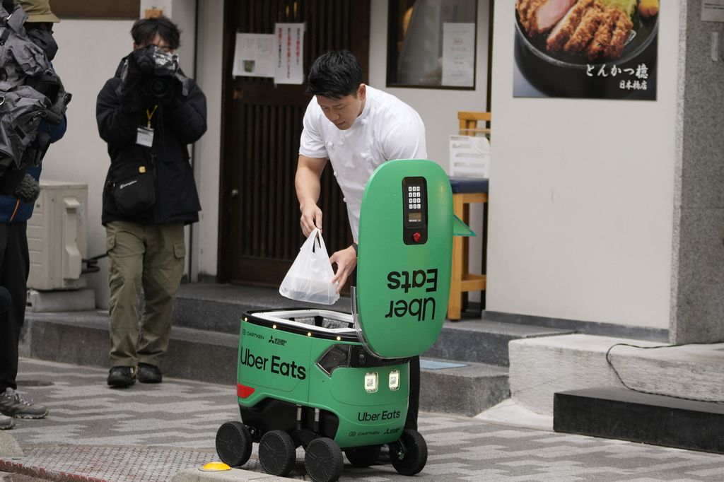 Seorang pekerja restoran memasukkan makanan dalam robot pengantar makanan Uber Eats saat demonstrasi untuk media di Tokyo, Jepang, Selasa (5/3/2024).