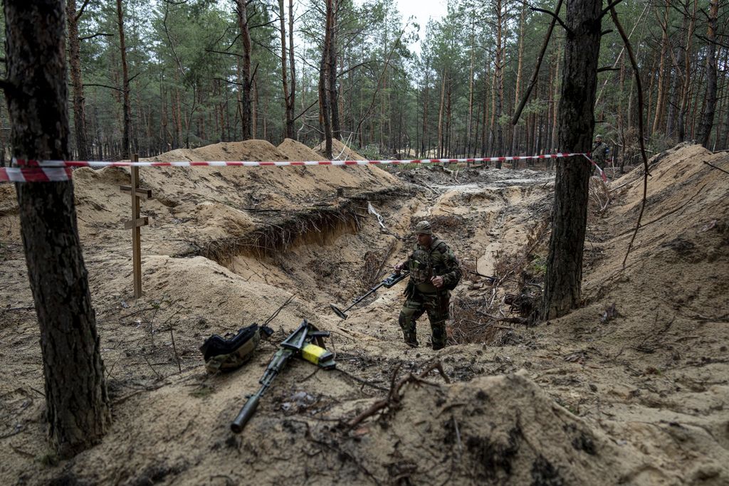 Seorang tentara Ukraina menggunakan alat pendeteksi metal untuk menyisir kuburan massal yang baru-barua ini ditemukan di Izium, Ukraina, Kamis (15/9/2022). Korban yang dikebumikan di lokasi itu adalah tentara Ukraina.