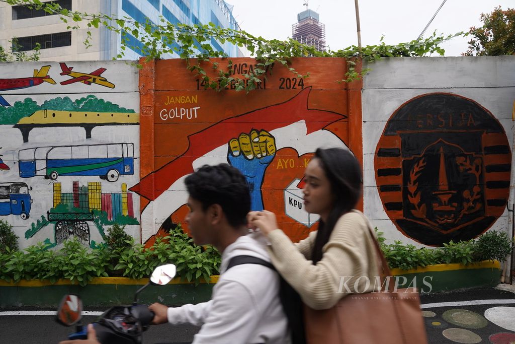 Karyawan perkantoran melintas di sekitar mural yang berisi ajakan datang ke tempat pemungutan suara untuk memilih dalam Pemilu 2024 di Kelurahan Kampung Bali, Tanah Abang, Jakarta Pusat, Rabu (7/2/2024). 