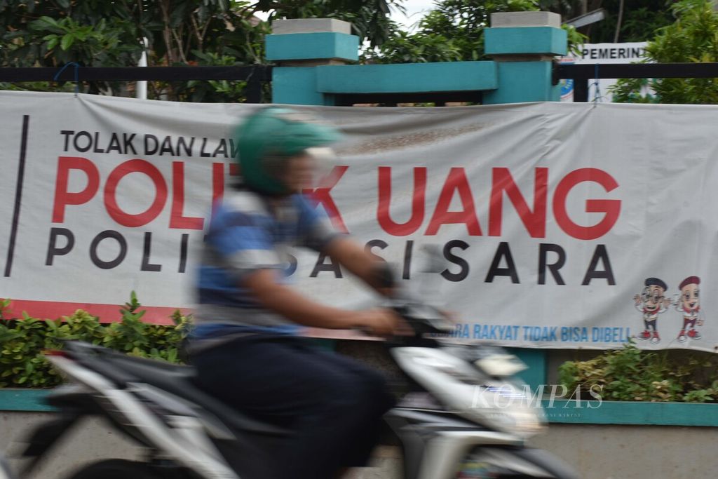 Seorang pengendara sepeda motor melintas di depan spanduk ajakan menolak praktik politik uang di Jalan Ceger Raya, Pondok Aren, Tangerang Selatan, Banten, Kamis (5/3/2020).