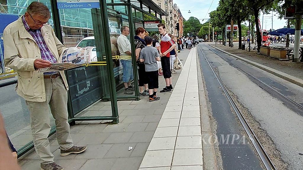 Membaca koran sambil menunggu angkutan umum di Stockholm, Swedia seperti terlihat tahun 2017. Kini sudah semakin jarang anak muda yang membaca koran cetak.