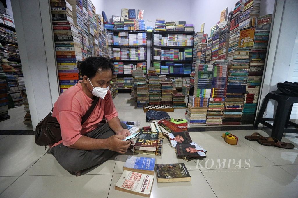 Nambela, seorang pedagang buku di Jakbook, Pasar Kenari, Jakarta Pusat, menyiapkan buku yang dibeli pelanggannya secara daring, Senin (27/12/2021). Berjualan buku secara daring melalui <i>marketplace </i>merupakan cara pedagang untuk bertahan.