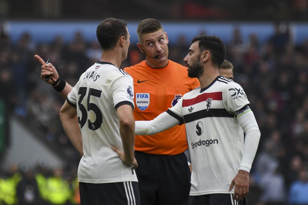 Bek Manchester United, Jonny Evans (kiri), berbicara dengan wasit Robert Jones (tengah) dan gelandang Bruno Fernandes saat laga Liga Inggris melawan Aston Villa di Villa Park, Birminghaim, Minggu (6/10/2024). 