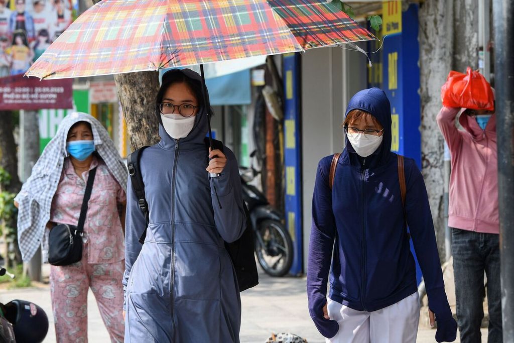 Dalam foto yang diambil pada 22 Mei 2023 ini tampak warga dengan menggunakan beragam pelindung, termasuk payung, berjalan di bawah terik matahari di jalanan kota Hanoi, Vietnam.