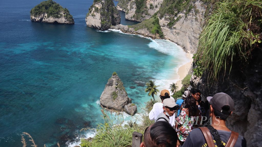 Wisatawan berjalan menuruni tangga di pinggir tebing menuju Pantai Diamond, di Pulau Nusa Penida, Kecamatan Nusa Penida, Kabupaten Klungkung, Bali, Rabu (23/3/2022). Wisatawan lebih banyak memanfaatkan keindahan pantai ini sebagai latar foto.