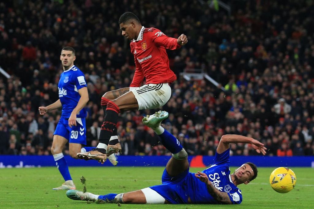 Penyerang Manchester United, Marcus Rashford (tengah), menghindari tekel gelandang Everton, Ben Godfrey (kanan), pada laga putaran ketiga Piala FA di Stadion Old Trafford, Manchester, Sabtu (7/1/2023) dini hari WIB. MU menang, 3-1.