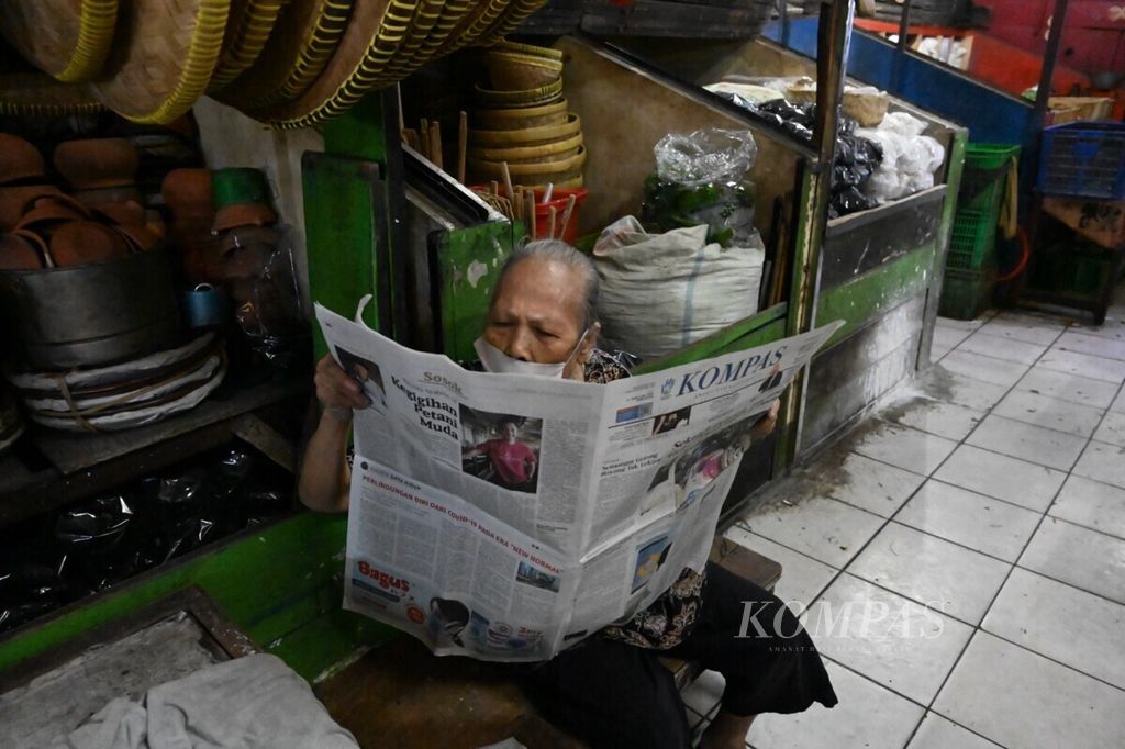 Heru Hartati (80), pedagang jamu di Pasar Palmerah, menunggu pembeli sambil membaca koran, Senin (13/7/2020).