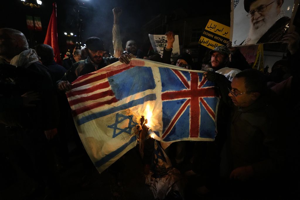 Demonstran Iran membakar gambar bendera Inggris, Amerika Serikat, dan Israel saat berunjuk rasa atas serangan militer AS dan Inggris terhadap kelompok Houthi di Yaman, di depan Kedutaan Besar Inggris di Teheran, Iran, Jumat (12/1/2024). 