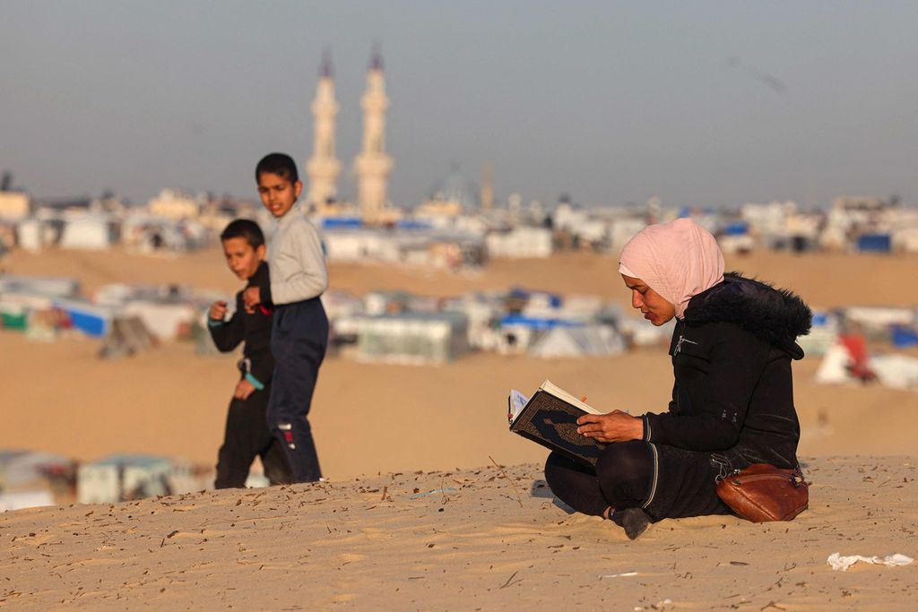 Seorang perempuan Palestina membaca Al Quran di dekat kamp pengungsi di Rafah, Jalur Gaza, saat hari pertama Ramadhan, 11 maret 2024.