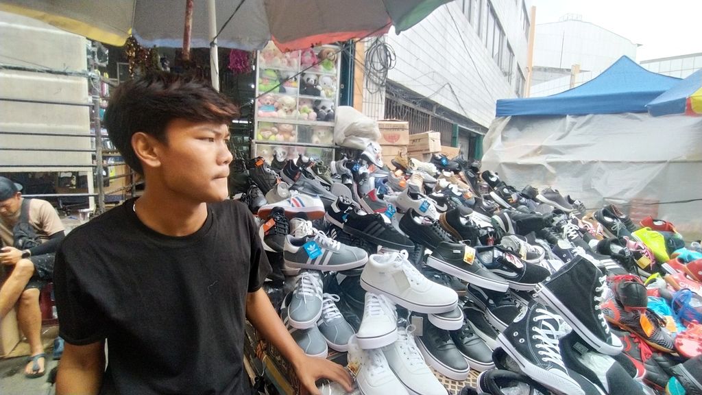 Adriansyah (18), pedagang sepatu asal Garut, menjajakan sepatu di Pasar Pagi Asemka, Jakarta Barat, Selasa (27/12/2022).