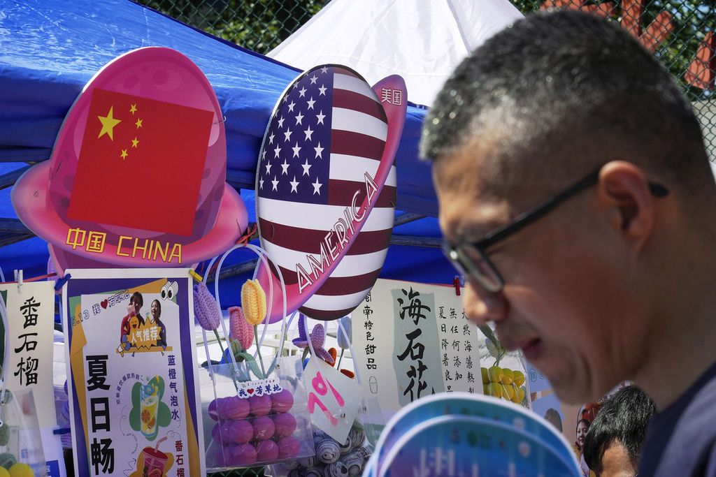 Seorang pria berjalan melewati kios yang menjual makanan dan minuman yang dijajakan di depan bendera China dan Amerika Serikat berbentuk planet saat karnaval musim panas di Beijing, China, 13 Mei 2023. 