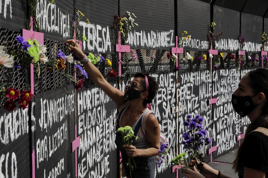 Aktivis perempuan menempatkan bunga di pagar pembatas yang didirikan di depan Istana Nasional dalam aksi menyambut Hari Perempuan Internasional di Mexico City, Minggu (7/3/2021).