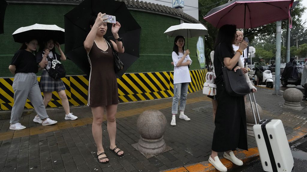 Warga menikmati hujan yang memberikan kesegaran dari terik musim panas di Beijing, China, Jumat (21/7/2023). 