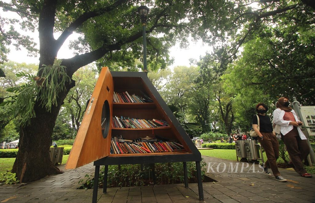 Pengunjung berjalan di dekat lemari buku Bookhive di Taman Suropati, Menteng, DKI Jakarta, Minggu (17/7/2022). Pengunjung dapat mengambil dan menitipkan buku di lemari itu. Kehadiran lemari tersebut mendekatkan akses terhadap bacaan di ruang publik.