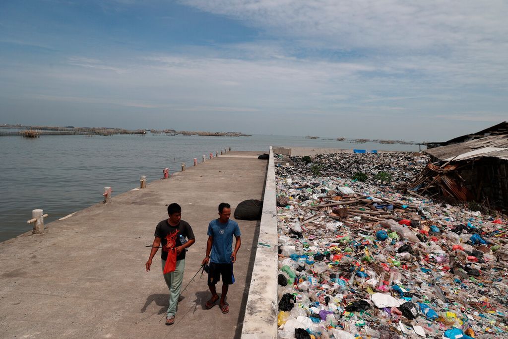 Warga melintasi tumpukan sampah yang dibuang di sekitar pesisir utara Kota Semarang, Jawa Tengah, Jumat (18/11/2022). 