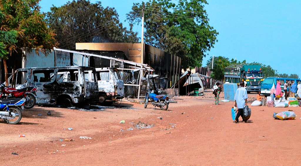 Orang-orang berjalan melewati kendaraan yang terbakar dan toko-toko yang dibakar kelompok Boko Haram di sebuah jalan di Benisheik pada 19 September 2013 setelah serangan mengerikan oleh kelompok Boko Haram yang menyamar dengan seragam militer di timur laut Nigeria.