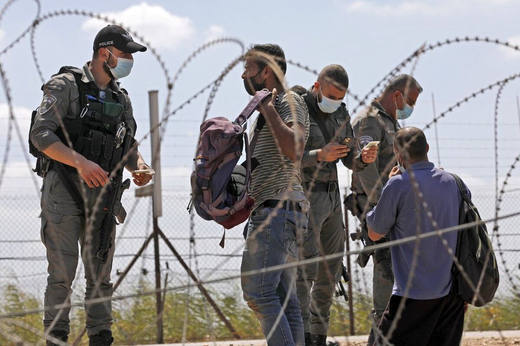 Pasukan keamanan Israel memeriksa dokumen pekerja warga Palestina sebelum mengizinkan mereka untuk menyeberang melalui lubang di pagar keamanan di desa Muqeibila dekat kota Jenin di Tepi Barat, Senin (6/9/2021).