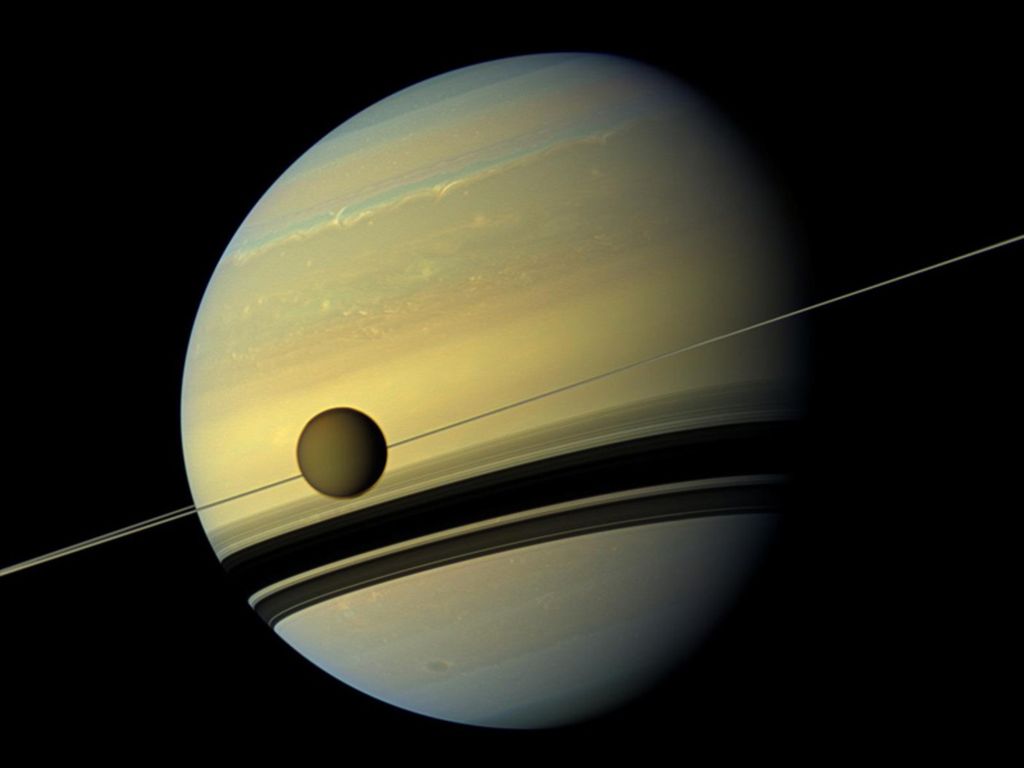 Bulan planet Saturnus, Titan, tampak dengan latar belakang Saturnus beserta cincinnya. Citra diambil oleh wahana Cassini milik  (NASA). Kondisi di Titan saat ini dianggap paling mirip dengan kondisi Bumi purba, sebelum kehidupan biologis muncul di Bumi. Titan merupakan salah satu kandidat kuat dunia di Tata Surya yang bisa menopang kehidupan. 