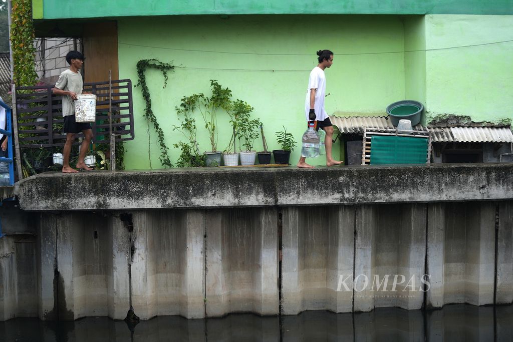 Warga menjinjing wadah berisi air bersih di Gang Bulak Cabe, RT 006 RW 009, Kelurahan Cilincing, Kecamatan Cilincing, Jakarta Utara, Jumat (1/12/2023). 