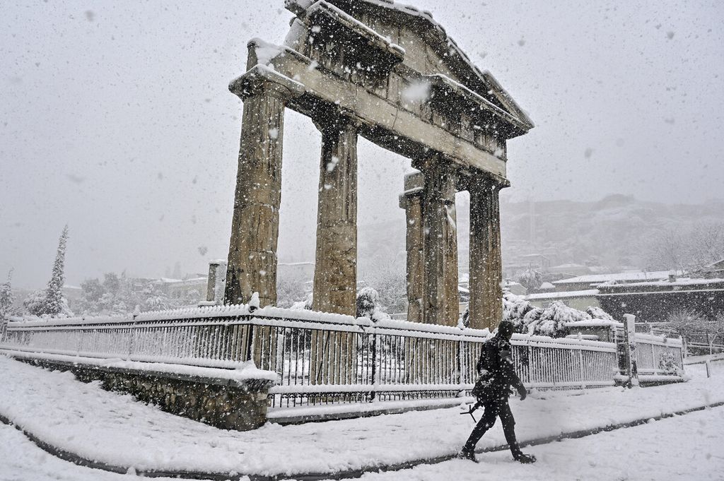 Seorang pria berjalan melewati Roman Agora saat hujan salju lebat di atas Athena, Yunani, Selasa (16/2/2021). 