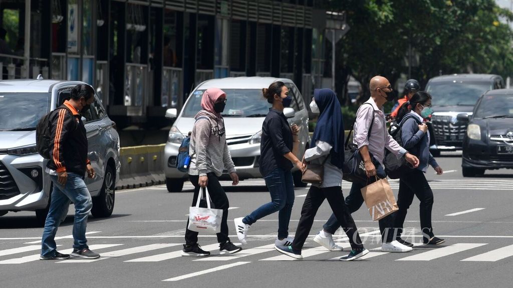 A number of office workers cross Jalan Sudirman to their workplace in the Sudirman area, Jakarta, on Monday (21/2/2022).