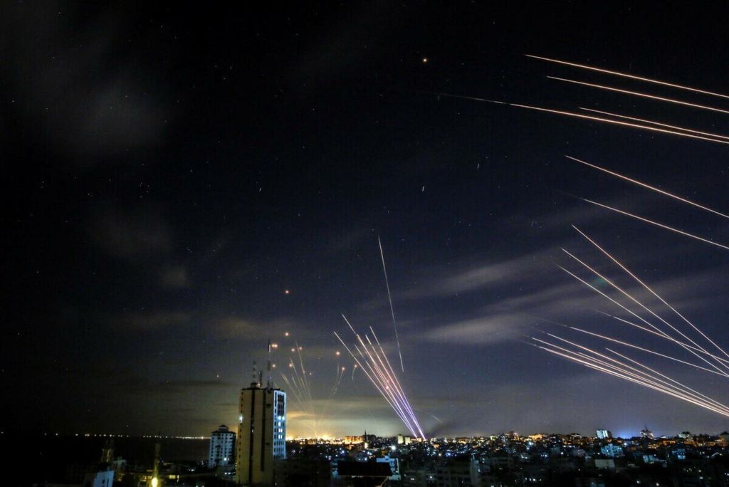 Sistem pertahanan rudal Iron Dome (kiri) mencegat roket (kanan) yang ditembakkan Hamas menuju Israel selatan dari Beit Lahia di Jalur Gaza utara. Di latar depan puluhan roket penyergap ditembakkan Hamas saat Iron Dome sibuk dengan roket pertama, seperti terlihat di langit di atas Jalur Gaza pada 16 Mei 2021. 