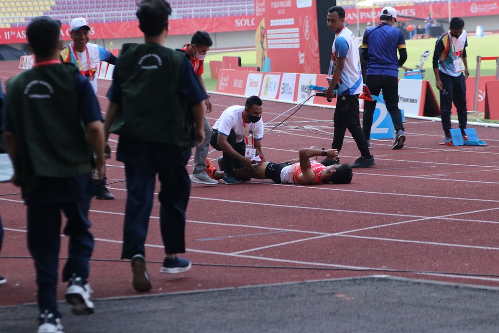 Sprinter Indonesia, Sapto Yogo Purnomo, telentang di lintasan akibat cedera <i>hamstring </i>paha kiri setelah finis terdepan di nomor 400 meter T37 ASEAN Para Games Surakarta 2022 di Stadion Manahan, Surakarta, Rabu (3/8/2022). Peraih medali perunggu 100 meter T37 Paralimpiade Tokyo 2020 itu kemudian mendapatkan perawatan dari fisioterapis.