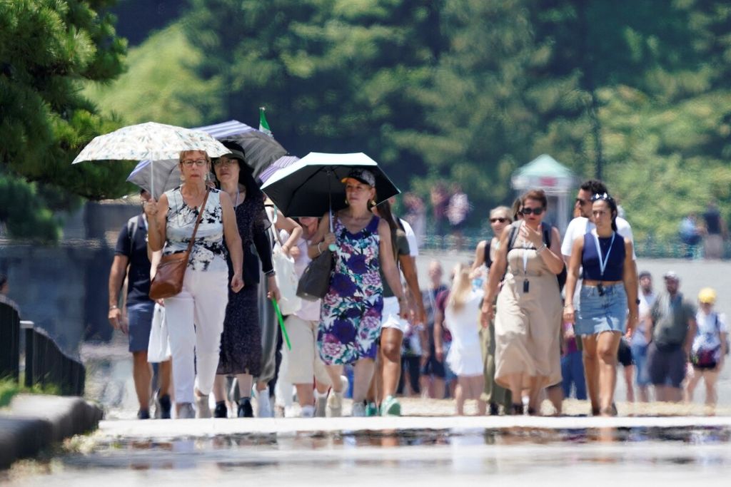 Turis asing berjalan di trotoar sepanjang Taman Istana Kekaisaran di tengah panas terik di Tokyo pada 12 Juli 2023.) 