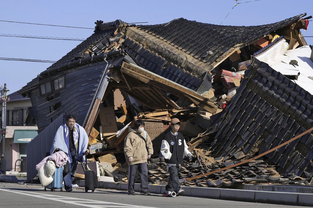 Warga, sambil membawa barang-barang miliknya, berjalan melewati rumah yang ambruk akibat gempa yang mengguncang Wajima, Prefektur Ishikawa, Jepang, Selasa (2/1/2024). 