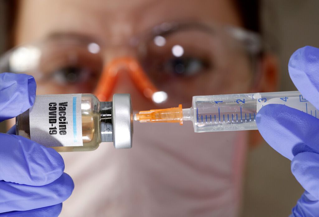 A woman holds a small bottle labbeled with a “Vaccine COVID-19” sticker and a medical syringe in this illustration taken April 10, 2020. 