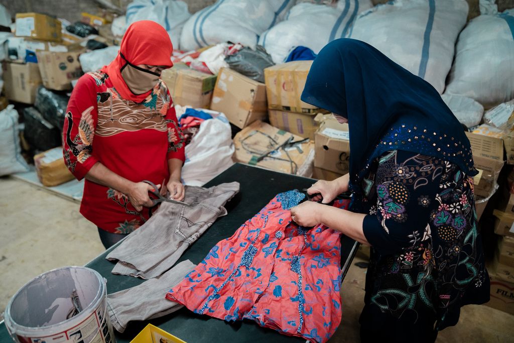 Dua orang ibu pekerja di pabrik daur ulang kain EcoTouch pada April 2022 di Jakarta dan Bandung, Jawa Barat. Mereka akan membongkar pakaian-pakaian utuh menjadi serat dan benang yang akan diproduksi kembali menjadi pakaian oleh Sejauh Mata Memandang.