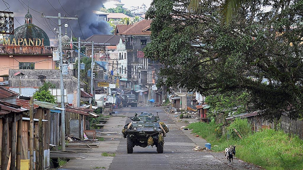 Kendaraan pengangkut personel milik Marinir Filipina menyusuri jalan, sementara asap hitam membubung dari rumah yang terbakar setelah helikopter militer menembakkan roket ke  tempat anggota kelompok ekstrem berada di kota Marawi, Pulau Mindanao, Filipina selatan, Selasa (30/5).  Kota itu ditinggalkan penduduknya setelah kelompok ekstrem mengusai sebagian wilayah Marawi.