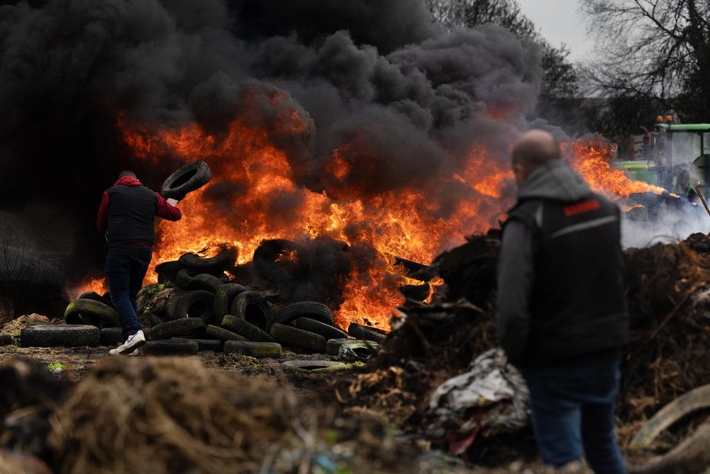Seorang petani melemparkan ban ke dalam api saat mereka berkumpul di bundaran sebagai bagian dari protes nasional para petani terhadap kebijakan pertanian di Plouisy, Perancis barat, 20 Februari 2024.