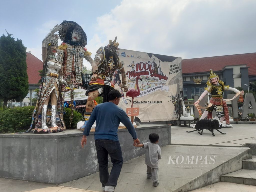 Pengunjung membawa anak kecil berjalan di dekat patung-patung yang terbuat dari sampah plastik yang dipamerkan pada event "1001 Manusia Sampah" di Balai Kota Among Tani, Kota Batu, Jawa Timur, Sabtu (23/7/2022).