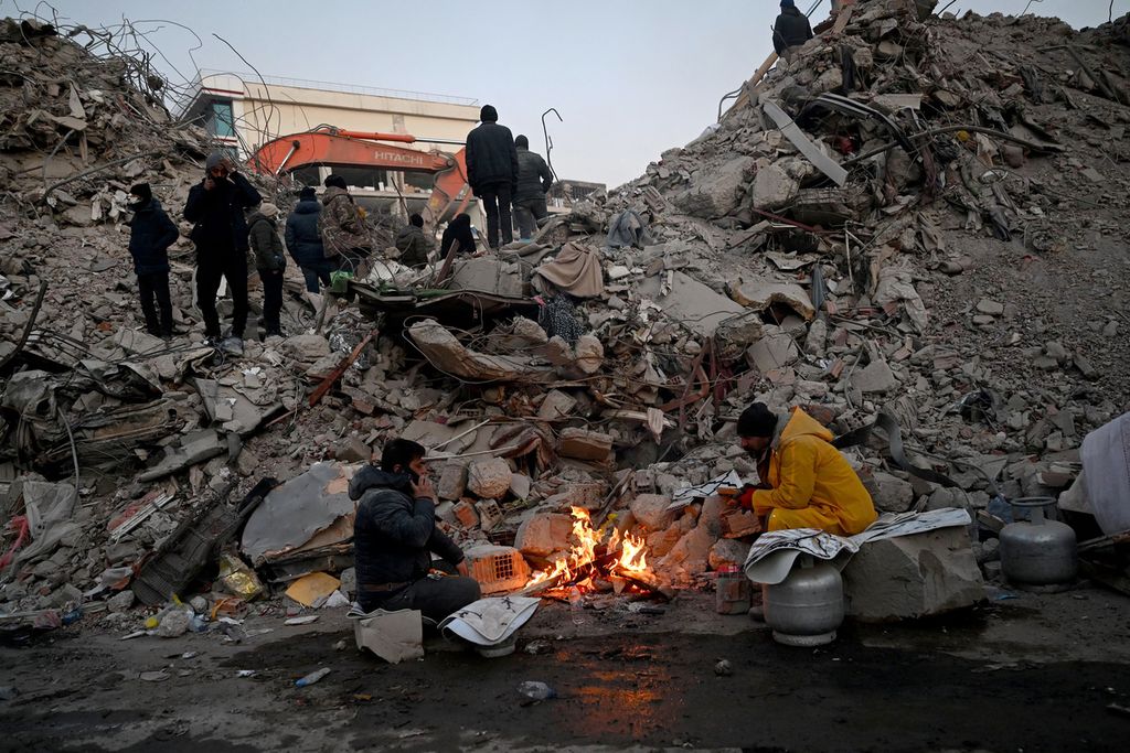Sejumlah warga menghangatkan diri di dekat api unggun yang menyala di depan reruntuhan bangunan yang rusak akibat gempa di Kahramanmaras, Turki, 12 Februari 2023.