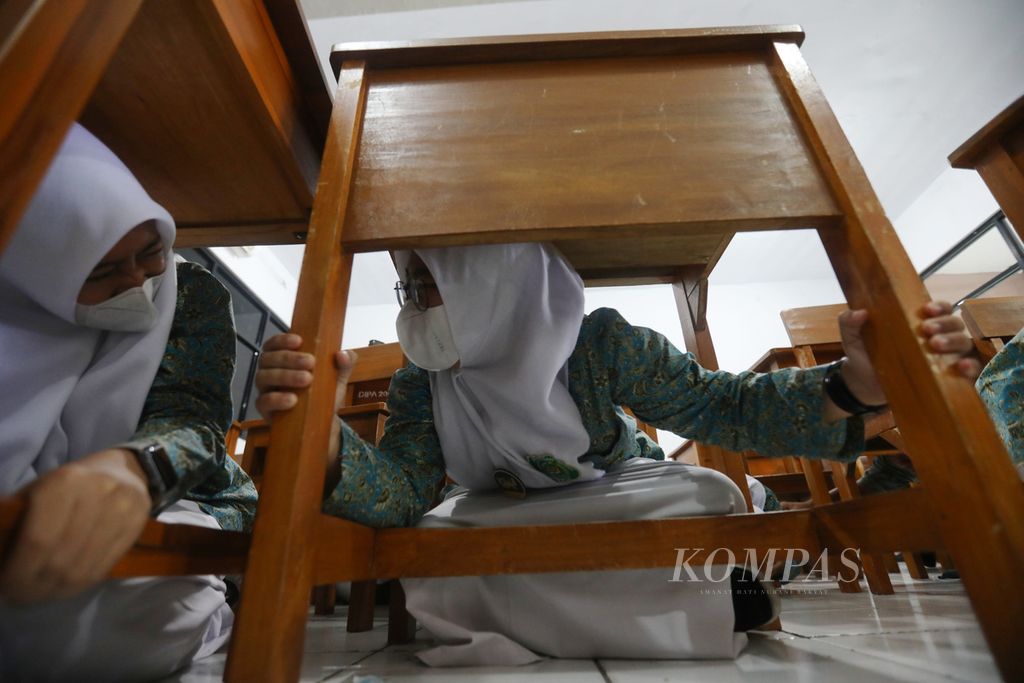 Siswa Madrasah Aliyah Negeri (MAN) 8 Cakung Timur, Jakarta Timur berlindung di bawah meja kelas saat mengikuti simulasi gempa bumi, Kamis (29/9/2022). 