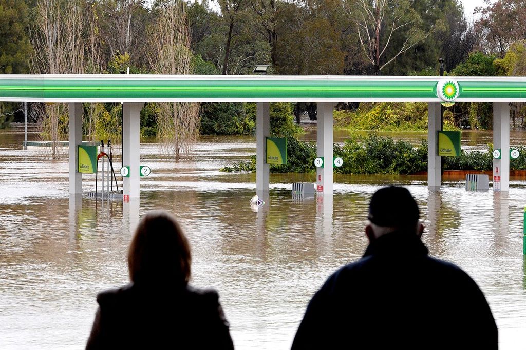 Warga berdiri di dekat stasiun pengisian bahan bakar untuk umum yang terendam banjir akibat hujan deras di Camden, pinggiran Sydney, Australia, 3 Juli 2022. 
