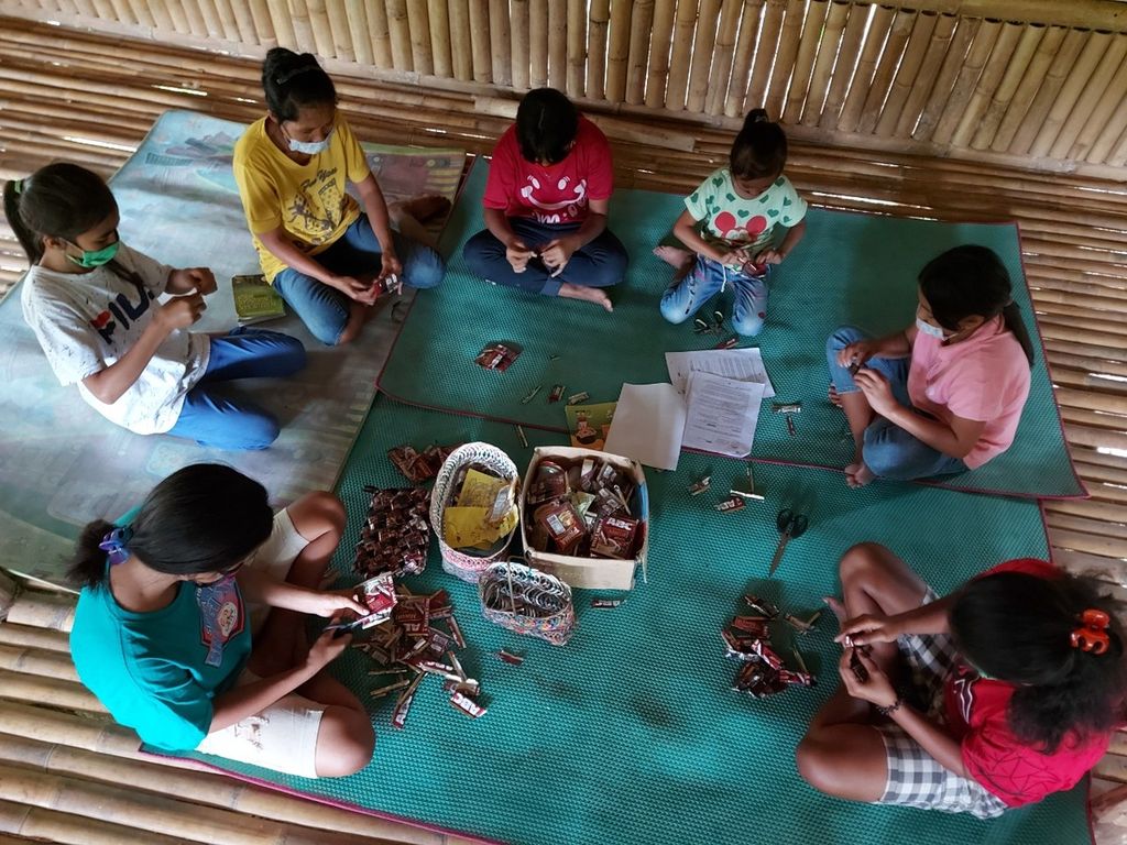 Anak-anak pekerja migran asal Sumba Barat Daya, Nusa Tenggara Timur, sedang merangkai wadah dari sampah kemasan kopi pabrikan di <i>umma pande</i> atau rumah pintar di Desa Welimbo, Kecamatan Wejewa Timur, Sumba Barat Daya. 