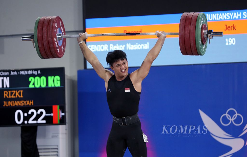 Lifter peraih emas angkat besi kelas 73 kg Olimpiade Paris 2024 asal Provinsi Banten, Rizki Juniansyah, tersenyum seusai menuntaskan angkatan <i>clean and jerk</i> berbobot 200 kg sekaligus mempertajam rekor nasional atas namanya sendiri dalam kesempatan ketiga pada cabang angkat besi kelas 89 kg PON Aceh-Sumut 2024 di Banda Aceh, Sabtu (7/9/2024).