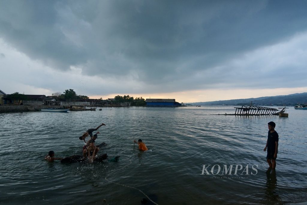 Di bawah langit hitam, anak-anak tetap berenang dan bermain di tepian Teluk Kendari, Kecamatan Abeli, Kendari, Sulawesi Tenggara, Kamis (16/12/2023). Cuaca buruk mengintai di tengah transisi musim hujan saat ini.