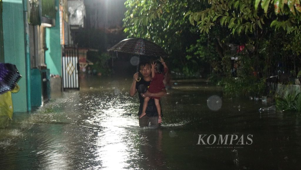 Warga menggendong anaknya sewaktu terjadi banjir, di Kelurahan Pucangsawit, Kecamatan Jebres, Kota Surakarta, Jawa Tengah, Kamis (16/2/2023). Banjir terjadi akibat hujan deras berjam-jam.
