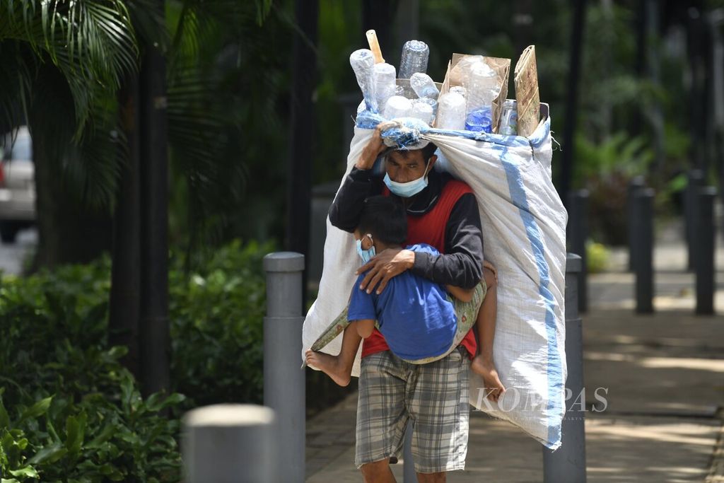 Pemulung yang berkeliling mengumpulkan botol bekas berjalan melewati jalur pedestrian di Jalan Kebon Sirih, Jakarta Pusat, Rabu (2/2/2022). Kenaikan inflasi bisa berdampak pada bertambahnya angka kemiskinan.