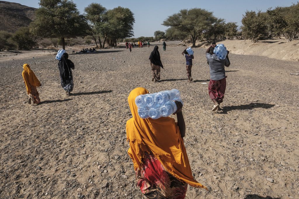 Perempuan pengungsi berjalan sambil menyunggi botol air mineral melintasi aliran sungai yang mengering di pinggiran desa Silse, 100 km dari Semera, Ethiopia, Selasa (15/2/2022). 