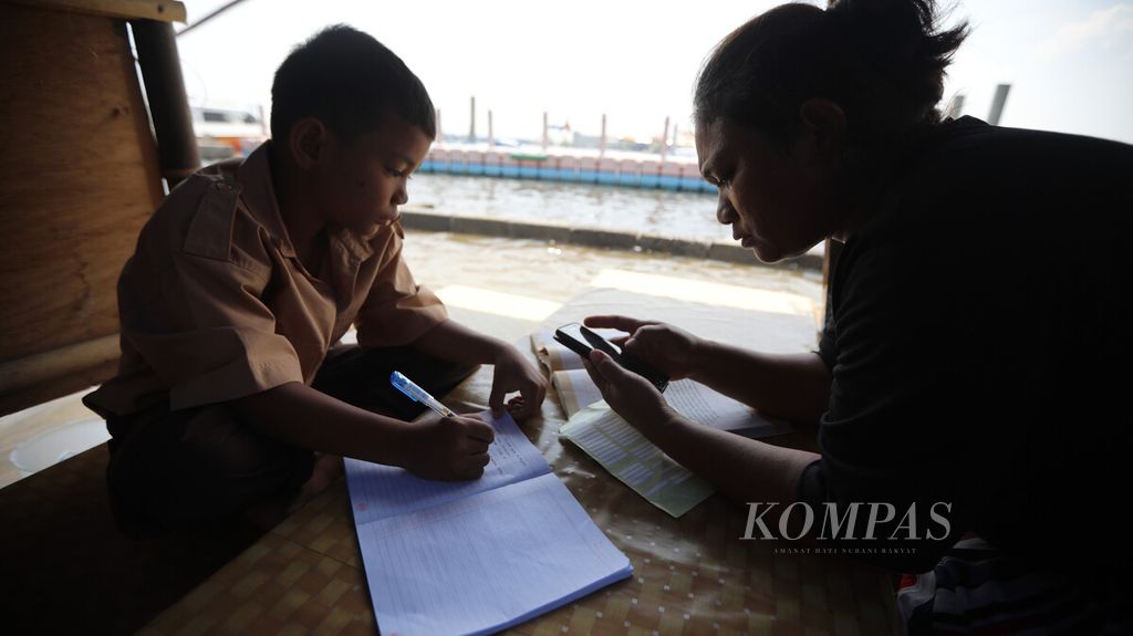 Seorang ibu membimbing anaknya saat pembelajaran jarak jauh di warungnya yang dikelilingi genangan banjir rob akibat air pasang di kawasan dermaga Pelabuhan Kaliadem, Muara Angke, Jakarta Utara, Rabu (21/10/2020).