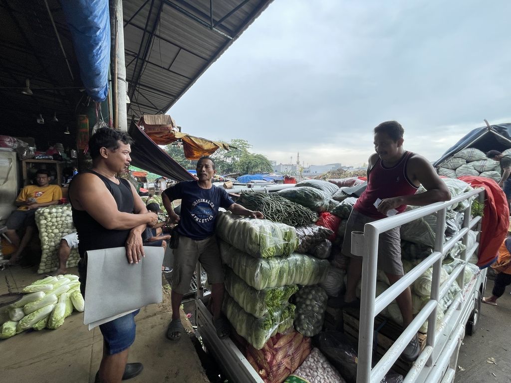 Syahroni (tengah) berbincang dengan dua teman sekelompoknya di depan pikap pembeli setelah mengangkut sayuran dari lapak di Pasar Induk Kramatjati, Jakarta Timur, Rabu (8/3/2023).