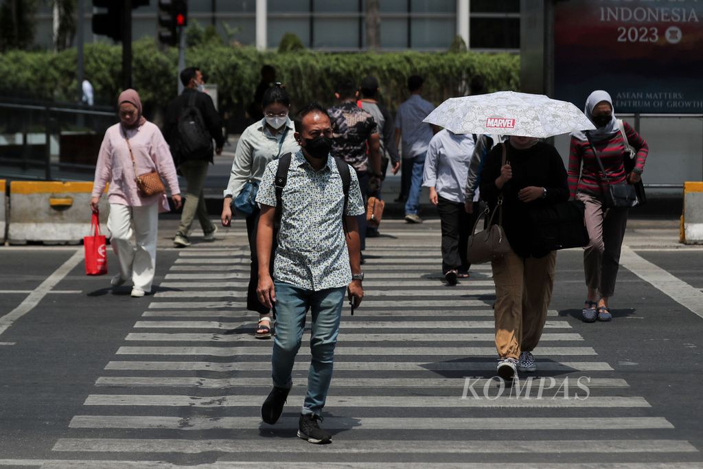 Seorang warga menggunakan payung saat menyeberang di kawasan Jalan MH Thamrin, Jakarta, Senin (9/10/2023). Suhu panas yang terjadi akhir-akhir ini diprediksi akan terus berlanjut hingga November 2023. 