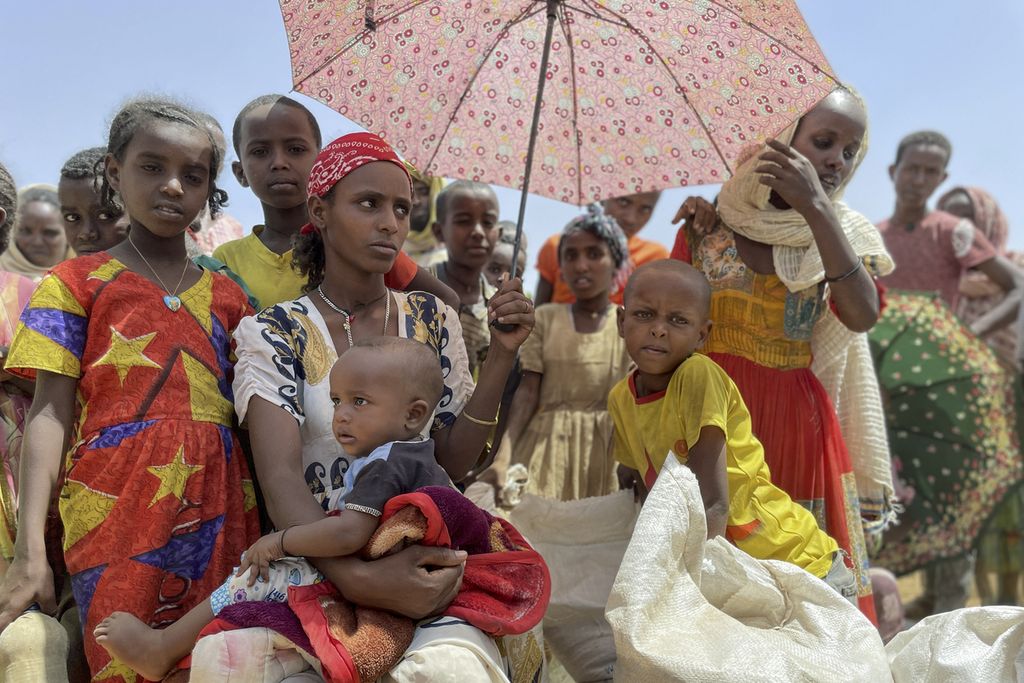 Perempuan dan anak-anak menunggu di bawah naungan payung di tempat distribusi makanan di kota Adi Mehameday, di wilayah Tigray barat Etiopia, Sabtu, 28 Mei 2022. Kelaparan mencengkeram jutaan orang di Etiopia, saat bersamaan harus menghadapi kombinasi konflik di utara dan kekeringan di selatan.