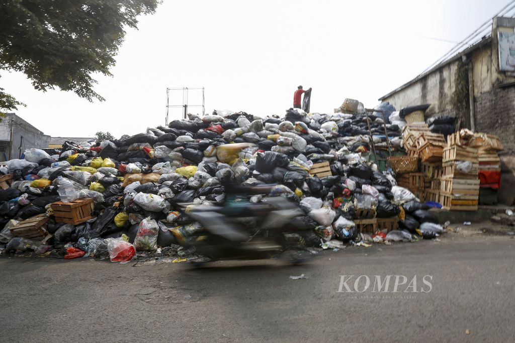 Pengendara sepeda motor melintas di samping tumpukan sampah di tempat pembuangan sementara (TPS) Pasar Gegerkalong, Kota Bandung, Jawa Barat, Rabu (11/10/2023). 
