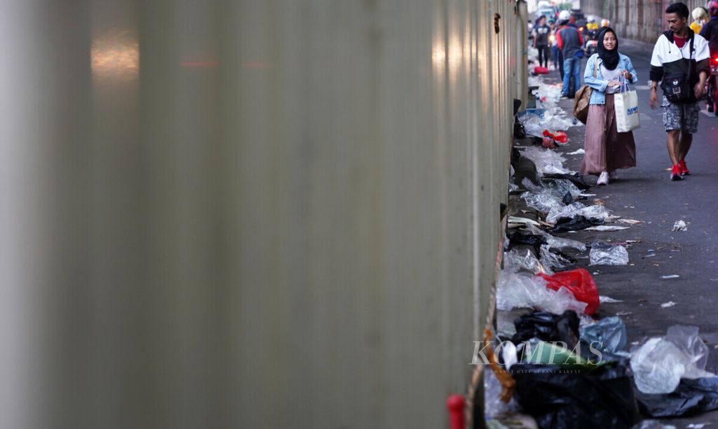 Warga melintasi serakan sampah plastik bekas pembungkus dagangan pedagang pakaian kaki lima Tanah Abang yang menggelar lapaknya di trotoar Jalan Jatibaru Raya, Tanah Abang, Jakarta, Minggu (2/6/2019).