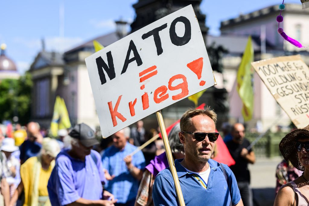 Pengunjung rasa membawa poster yang pesannya berarti "NATO sama dengan perang" dalam demonstrasi yang mendesak pemerintah Jerman tidak ikut campur dalam Perang Ukraina, di Berlin, Sabtu (2/7/2022).  